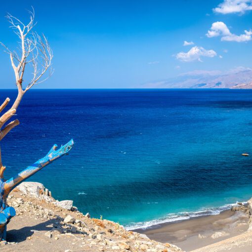 Pohľad z útesu na zátoku pri pláži Agios Pavlos, kde sa šedé piesočnaté duny zvažujú do priezračne modrého mora. Pokojné miesto obklopené skalnatým pobrežím patrí k najkrajším častiam južnej Kréty.