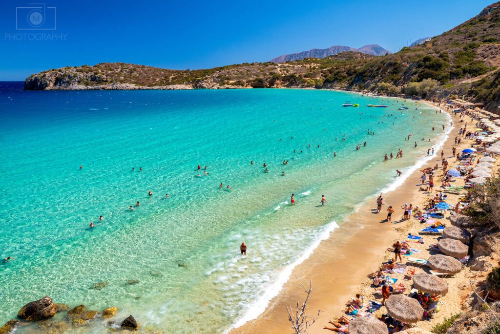 Voulisma Beach na Kréte s tyrkysovou vodou, pieskovou plážou a ľuďmi na severovýchode ostrova